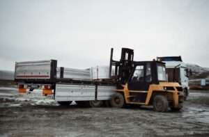 Forklift loading materials onto a truck in an industrial landscape.