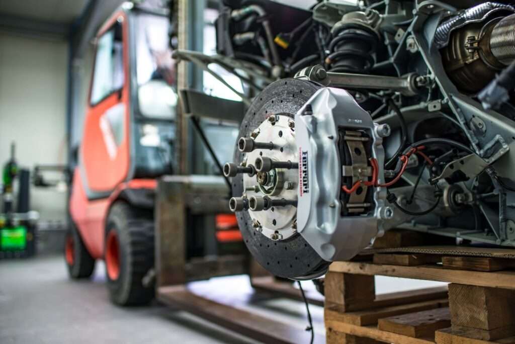 Detailed view of an automotive brake caliper and disc in an industrial workshop setting.