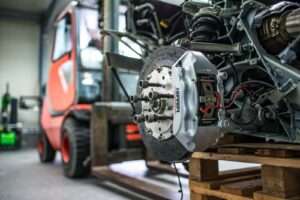 Detailed view of an automotive brake caliper and disc in an industrial workshop setting.