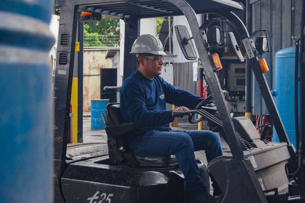 An industrial worker wearing protective gear operates a forklift inside a warehouse.