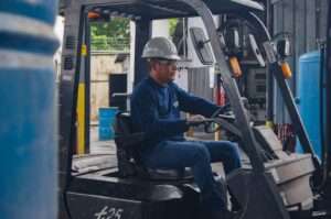 An industrial worker wearing protective gear operates a forklift inside a warehouse.